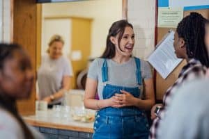 A woman in dungarees talks to another person at a community centre