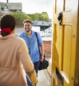 A woman opens her front door to a healthcare worker